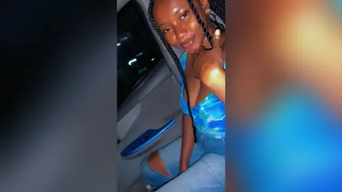 Smiling young woman in a blue patterned tank top sitting in a car at night.