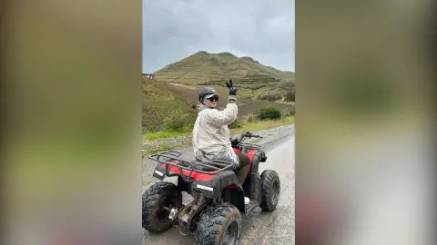 Adventurous woman in white jacket riding a red ATV on a mountain road under a cloudy sky.