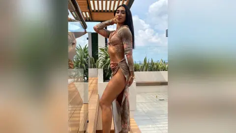 Fashionable woman in a brown cutout maxi dress posing on a sunny luxury balcony.
