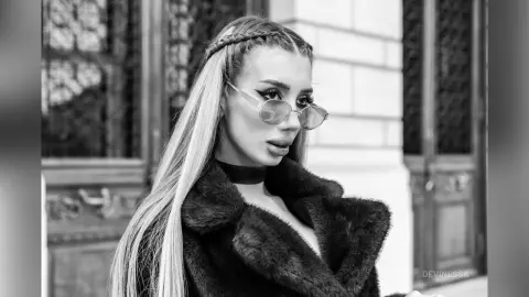 DeviNessa poses in a black fur coat and sunglasses with her long hair styled in a thick braid.