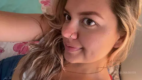 Smiling young woman with blonde hair and nose ring relaxing in a cozy bedroom setting.