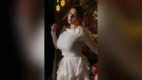 Young woman in a white long-sleeve top and ruffled skirt posing by festive Christmas lights and decorations.