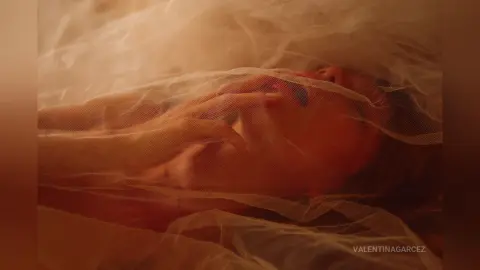 Dreamy close-up of a woman lying under sheer white tulle fabric in a soft, ethereal mood.