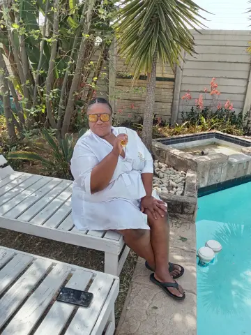 Relaxed woman in a white linen outfit sitting by a backyard swimming pool on a sunny day.