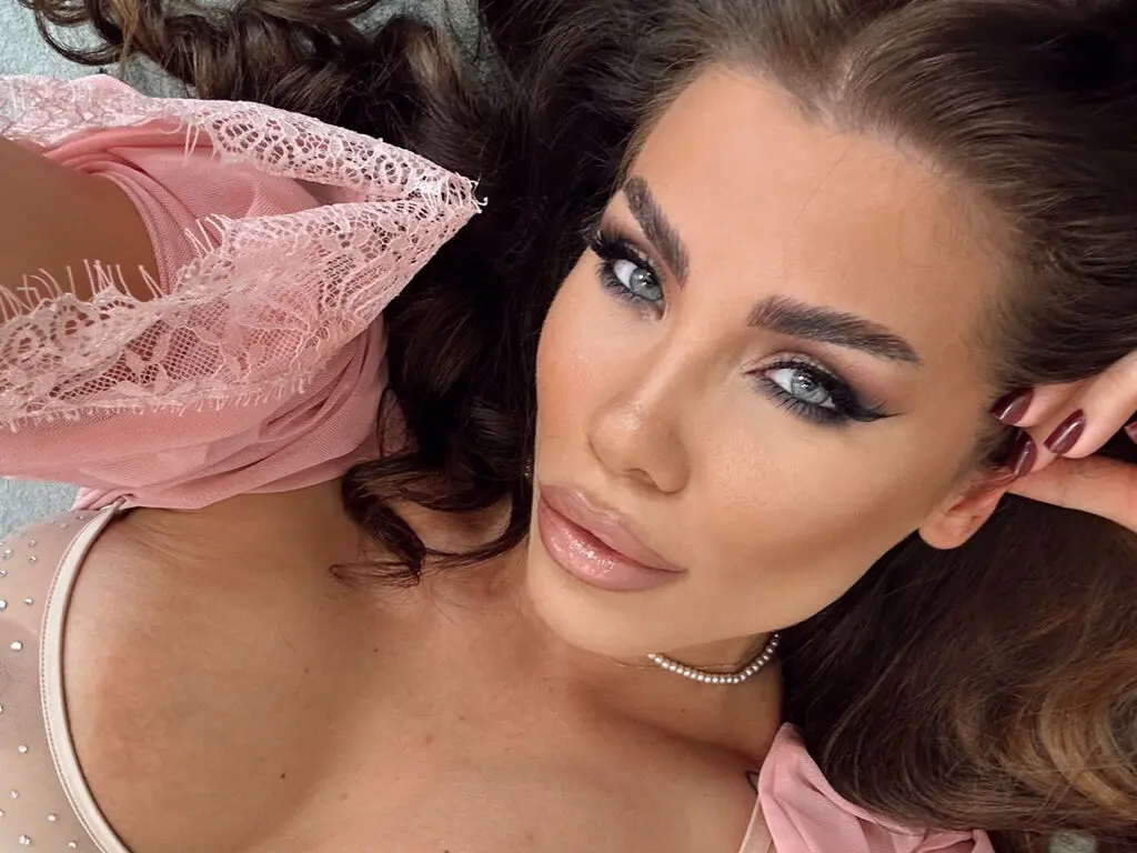 Close-up portrait of a glamorous woman with winged eyeliner wearing a pink lace blouse in a soft, dreamy mood.