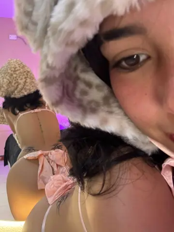 Young woman in a fuzzy leopard print hat and pink lingerie posing in a warm, dimly lit room.