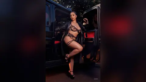 Confident woman in black lace lingerie and leather jacket posing in a luxury black SUV at night.