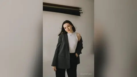 Young woman in a chic dark blazer and white tank top posing in a minimalist modern room.