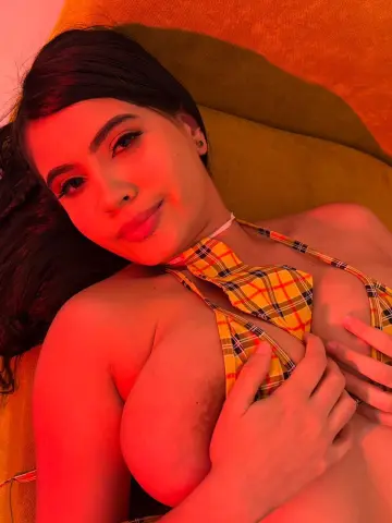 Young woman in a yellow plaid bikini relaxing on a warm orange sofa under soft red lighting.