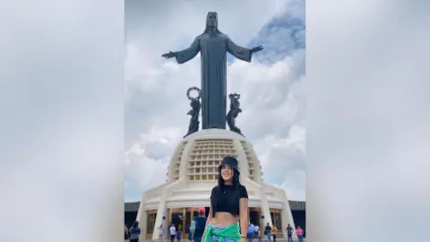 Smiling woman in a black crop top and bucket hat standing before the Christ the Redeemer statue in Rio de Janeiro.