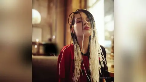 VikkiCominsky poses with long blonde and black dreadlocks wearing a red shirt.