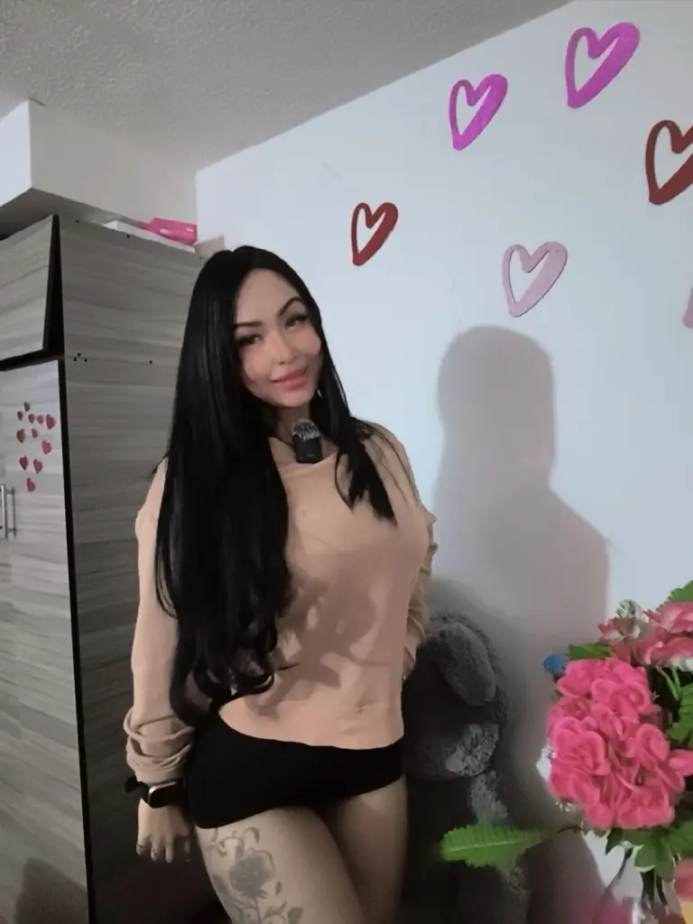 Gabilicious25 — Smiling woman with long black hair wearing a beige sweatshirt in a room decorated with pink heart wall decals.