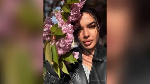 Beautiful woman in a black leather jacket holding pink lilac flowers in a sunny garden setting.