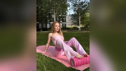 Young woman in pink yoga outfit relaxing on a mat in a sunny green park.