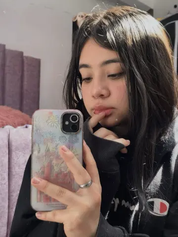 Young woman with long dark hair taking a moody selfie in a black hoodie using a floral patterned phone case.