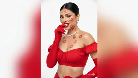 Glamorous woman in a red off-the-shoulder crop top and matching gloves with red lipstick kiss marks on her skin.