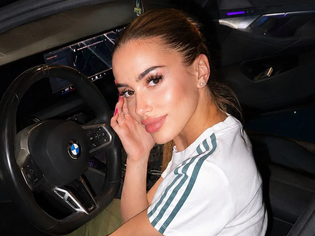 MarissaFox sits in the driver's seat of a car wearing a white t-shirt with green stripes.