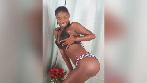 Smiling Black woman in colorful patterned bikini posing against a light green backdrop.