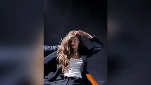 LissaDesso poses with her long wavy hair while wearing a white top and a black blazer against a dark background.