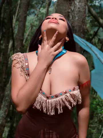 Dreamy portrait of a woman in a fringed brown costume posing in a lush green forest setting.