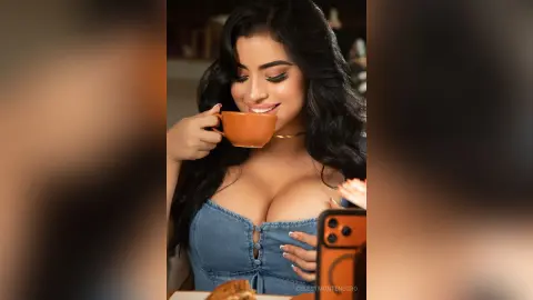 Beautiful woman in a denim top sipping coffee in a cozy cafe setting.