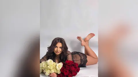 Young woman in black lace lingerie lying on a white floor with red and white roses in a romantic mood.