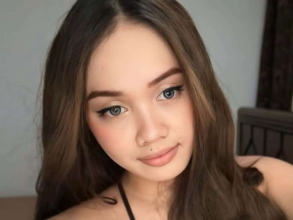 MaxCiana poses with long brown hair and light eye makeup, looking directly at the camera with a slight smile.
