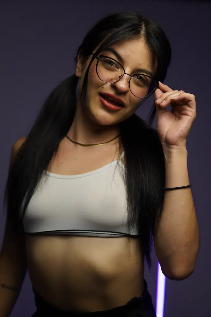 abbytheran poses in a black strapless top and bunny ears, showing her long dark hair and smiling against a dark background.