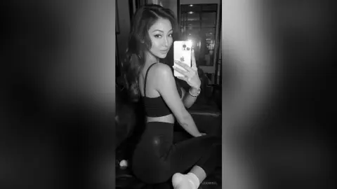 LeahReel — Young woman in black sports bra and leggings taking a moody black and white mirror selfie indoors.