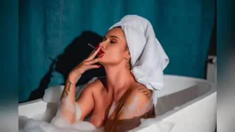 Relaxed woman in a white towel relaxing in a bubbly bathtub against a teal background.