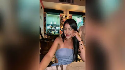 Smiling young woman in a blue strapless top sitting at a restaurant table with a joyful mood.