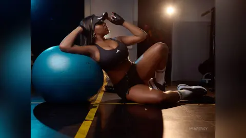 Fit woman in black gym wear relaxing on a blue exercise ball in a moody, dimly lit home workout space.