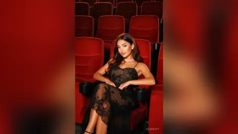 Elegant woman in a black lace dress sitting in red cinema seats with a sophisticated mood.