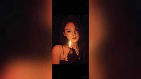 Moody portrait of a woman in a black dress holding a lit lighter in a dark, warm-toned setting.
