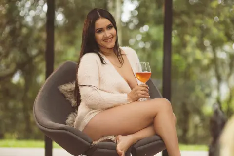 Smiling woman in a cozy white sweater relaxing outdoors with a glass of rosé wine.