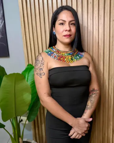 Woman in a black strapless dress and colorful beaded statement necklace posing against a wooden slat wall.