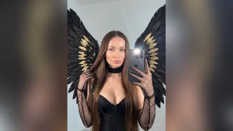 Woman in black corset and sheer sleeves wearing large black and gold angel wings for a dramatic photoshoot.