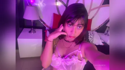 Young woman in white lace lingerie posing in a bedroom with moody purple lighting.