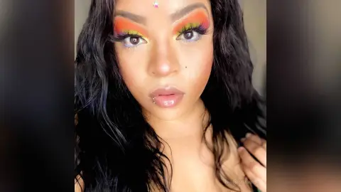Close-up portrait of a woman with colorful rainbow eye makeup and long wavy black hair in a soft studio light.