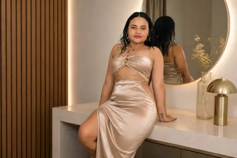 Elegant woman in a champagne satin cutout maxi dress posing in a modern, minimalist interior setting.