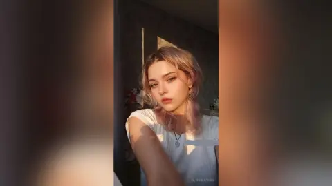 Young woman with blonde hair in a white t-shirt posing in warm, golden hour sunlight.