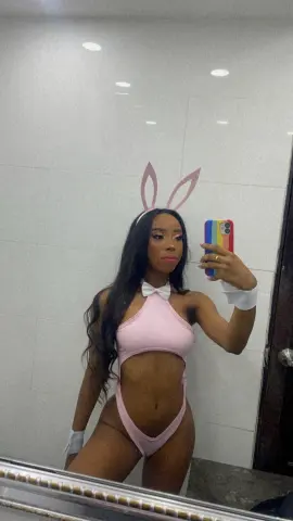 Young woman in a pink bunny costume and white bow posing for a mirror selfie in a modern bathroom.