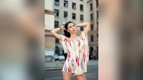 Stylish woman in a white patterned romper posing confidently on a city street during golden hour.