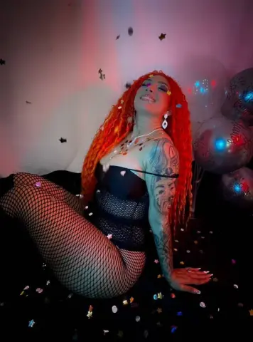 Redheaded woman in black bodysuit and fishnets posing with balloons in a festive, celebratory mood.