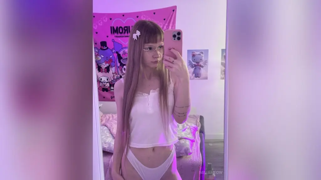Young woman with blonde bangs and floral headband in soft pink aesthetic lighting.
