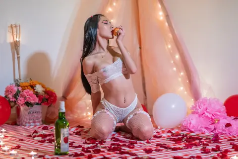 Young woman in white lace lingerie kneeling on a romantic rose petal floor near balloons and flowers.