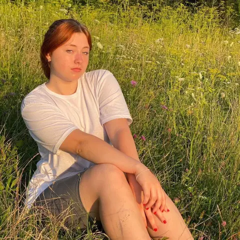 Young woman in a white t-shirt sitting peacefully in a sunny wildflower meadow during golden hour.