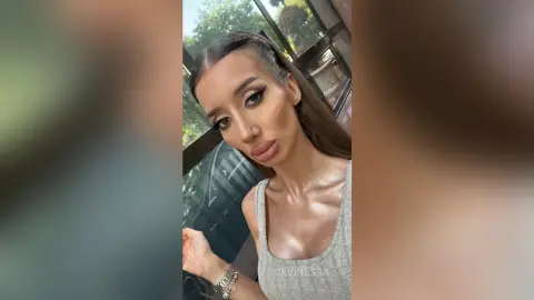 DeviNessa poses in a grey tank top with her long brown hair slicked back and styled away from her face.