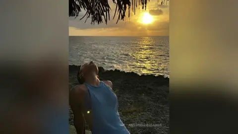 Woman in a blue sleeveless top relaxing by the ocean during a golden sunset.