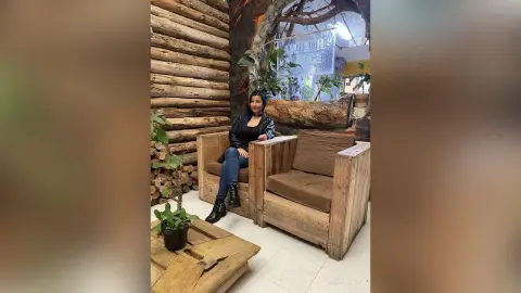 Woman in black leather jacket and jeans sitting in a rustic wooden lounge with a cozy cabin atmosphere.